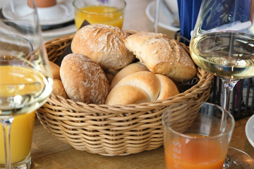 A basket of bread and a glass of orange juice sit on a table