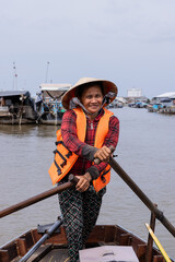 Vertical photo of a Vietnamese woman wearing an orange life jacket while she is navigating through the floating market in the mekong delta