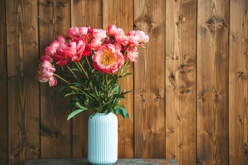 A beautiful display of pink peonies in a white ribbed vase set against a wooden backdrop with copy-space