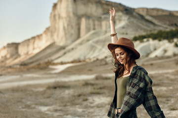 empowered woman in plaid shirt and hat with outstretched arms against majestic mountain backdrop