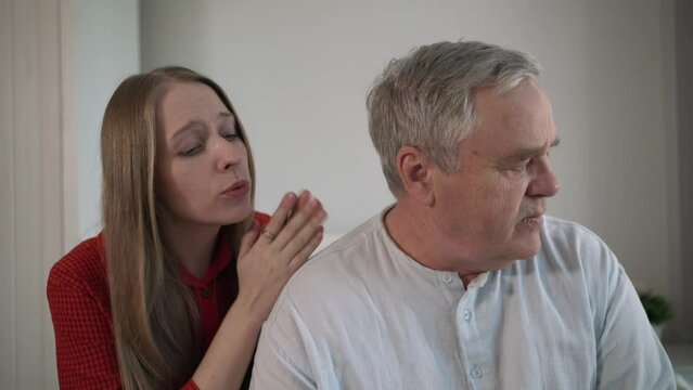Young woman comforting elderly man by putting hands on his shoulders. Emotional support and care between different generations, demonstrating compassion and empathy in domestic setting.