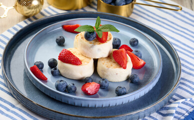 Round small fried cheesecakes on a blue plate with berries. Healthy breakfast