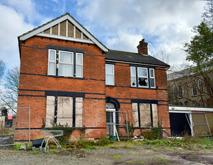 A derelict detached house with boarded up windows downstairs and a broken window upstairs. 