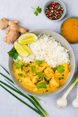 Curry sauce with chicken and rice in a plate, lime, spices and herbs on a light background, top view. Traditional Indian dish.
