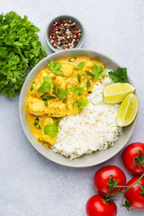 Curry sauce with chicken and rice in a plate, lime, tomatoes, spices and herbs on a light background, top view. Traditional Indian dish.