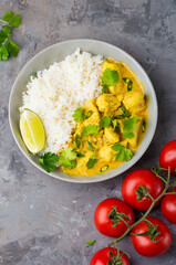 Curry sauce with chicken and rice in a plate, lime, tomatoes, spices and herbs on a dark background, top view. Traditional Indian dish.