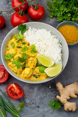 Curry sauce with chicken and rice in a plate, lime, tomatoes, spices and herbs on a dark background, top view. Traditional Indian dish.