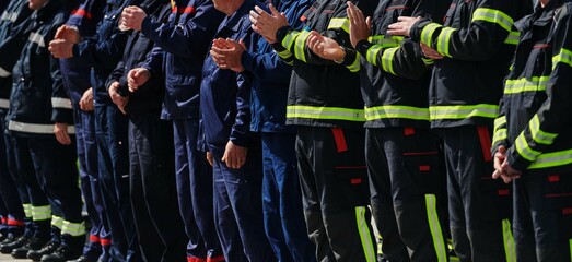 A group of firefighters lined up, saluting the flag, applauding in solidarity, and gearing up for...