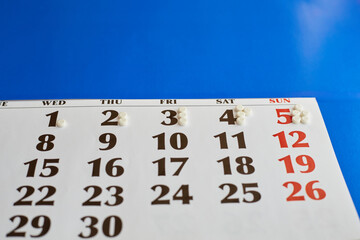Obraz premium Tablets white pills on calendar on blue background closeup, taking a large dose of medication daily, increasing dose of medication