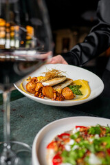 A close-up of a gourmet dish being served in an elegant restaurant, with a focus on the plated food and a blurred background enhancing the fine dining experience