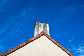 Cheminée blanche sur un toit aux tuiles rouge clair avec ciel bleu en fond.