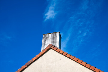 Cheminée blanche sur un toit aux tuiles rouge clair avec ciel bleu en fond.