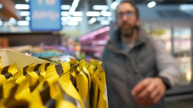 A male buyer takes a granola bar from the shelf of a supermarket close-up