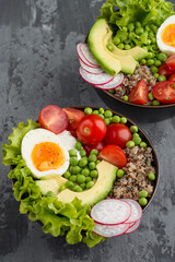 Bowl with healthy salad of quinoa, avocado, legumes, herbs, cherry tomatoes, egg and cream cheese on a dark background. View from above. The concept of proper nutrition, self-care and health.