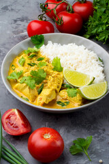 Curry sauce with chicken and rice in a plate, lime, tomatoes, spices and herbs on a dark background. Traditional Indian dish.