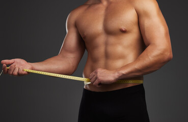 Stomach, body and fitness man in studio with measuring tape for bodybuilding abs, goals and progress on black background. Muscle, sports and male athlete with sixpack measurement, growth or tracking