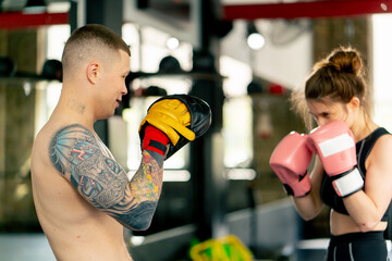 close u pin a boxing fight club a young girl in a black sweatshirt with pink gloves practices with...