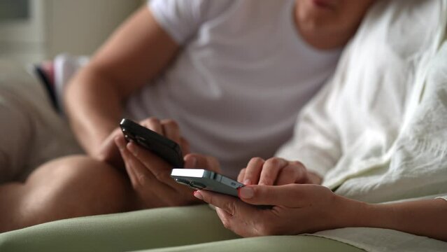 Relaxed young couple tapping together smartphone screen to farming new popular Hamster Kombat cryptocurrency in mobile phone online application, sitting on sofa at home. Shooting in slow motion.