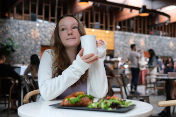 Portrait of a beautiful, young, thoughtful girl in a cafe, with a white cup in her hands, coffee, tea