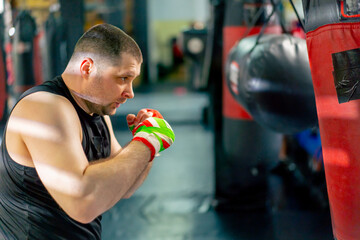 close up in a boxing fight club senior muscular trainer in a black T-shirt and with multi-colored...