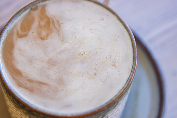 Top view of white cream foam slowly dissolving in the black coffee rotating and mixing in the...