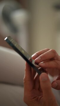 Closeup vertical shot of unrecognizable man tapping fingers on mobile phone screen to farming new Hamster Kombat crypto coin in Telegram application. Shooting in slow motion.