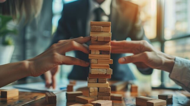 closeup of people playing jenga tower block game, teamwork and collaboration concept