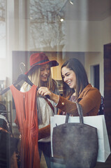 Customer, smile and women with dress in boutique shop for promotion, sale and discount. Happy, female friends and people checking rack of clothes in fabric, fashion and retail store at indoor mall