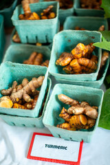 Multiple green cardboard containers with turmeric roots or Curcuma longa,  on a table at a market. There's a white paper sign with red trim and black lettering. The spice is  anti-inflammatory food.