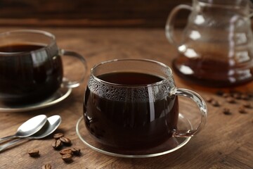 Hot coffee in glass cups, spoons and beans on wooden table, closeup