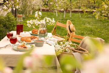 Stylish table setting with beautiful spring flowers, fruit drink and pie in garden