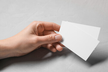 Woman holding blank cards at light grey table, closeup. Mockup for design