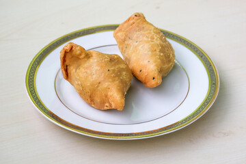 Two fried samosas on a white plate. It is also known as singara, singada, samose, somsa, sambusa, and samuza. Traditional street food from Bangladesh and the Bengal region of India.