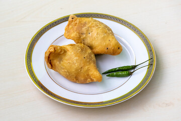 Bengali street food fried singara or samosa served on a white plate with twogreen chilies. It is also known as singada, samose, somsa, sambusa, and samuza.