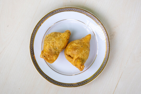 Two fried singara or samosas on a white plate on light wooden surface. Top view.