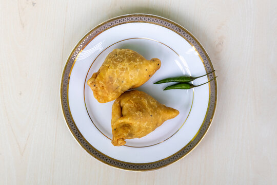 Bengali street food fried samosa or singara served on a white plate with twogreen chilies. Top view.