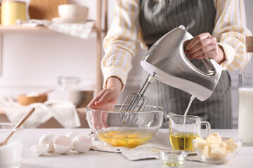 Woman making dough with mixer in bowl at table, closeup