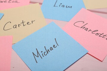 Paper stickers with different names on pink wooden table, closeup. Choosing baby's name
