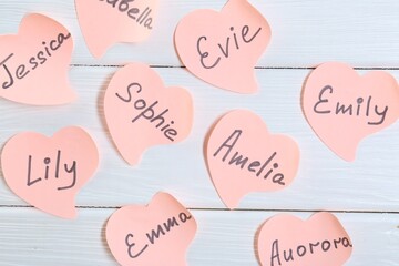 Paper stickers with different names on white wooden background, flat lay. Choosing baby's name
