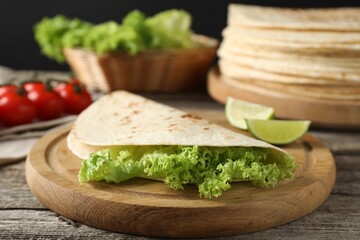 Tasty homemade tortillas, lettuce, lime and tomatoes on wooden table, closeup