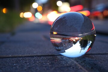 Beautiful city street, overturned reflection. Crystal ball on asphalt road outdoors, closeup. Space...
