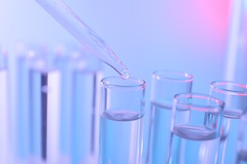 Dripping liquid from pipette into test tube on color background, closeup
