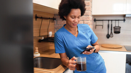 African American nurse drinking morning coffee and using smartphone before work