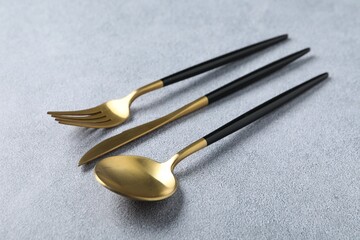 Stylish golden cutlery. Fork, spoon and knife on grey table