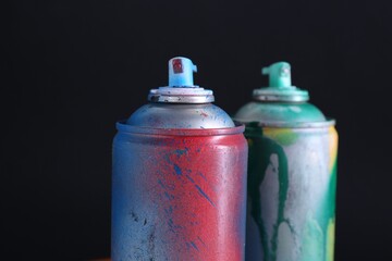 Two spray paint cans on dark background, closeup