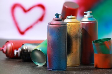 Many spray paint cans on gray surface against color background