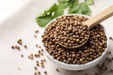 Dried coriander seeds in bowl and spoon on light cloth, closeup