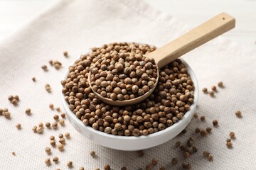 Dried coriander seeds in bowl and spoon on light cloth , closeup