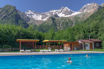 A heated pool high in the mountains. Relaxing by the water in the fresh air. Sun loungers for relaxing and sunbathing near the blue water pool. Vacation in the mountains in summer.