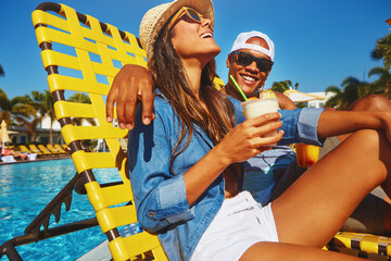 Couple, poolside and alcohol for fun on holiday, outdoor and travel to hotel resort for vacation. People, peace and sunglasses by water for drinks, bonding and love by swimming pool for wellness